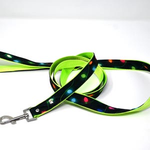 May include: A black and green dog leash with a neon green trim. The leash has a pattern of colorful lights on it.