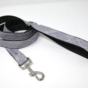 May include: A gray and white plaid dog leash with a black backing and a silver clip.