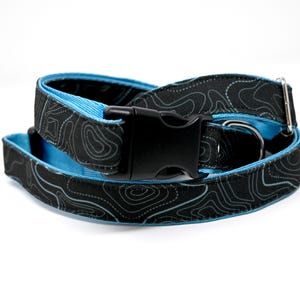 May include: A black and blue dog collar with a topographic pattern. The collar has a black buckle and a silver D-ring.