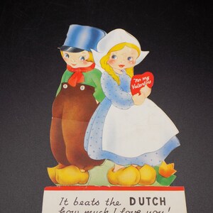 May include: A vintage Valentine's Day card featuring a cartoon couple dressed in Dutch clothing. The woman is holding a red heart that says "For my Valentine". The card reads "It beats the DUTCH how much I love you!"