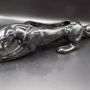 May include: Black ceramic panther planter. The panther is in a crouching position with its head turned to the side. The planter has a hollowed-out back for planting.