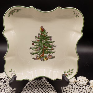 May include: A white ceramic serving dish with a green rim and a Christmas tree design. The tree is decorated with ornaments and presents. The dish has a scalloped edge.