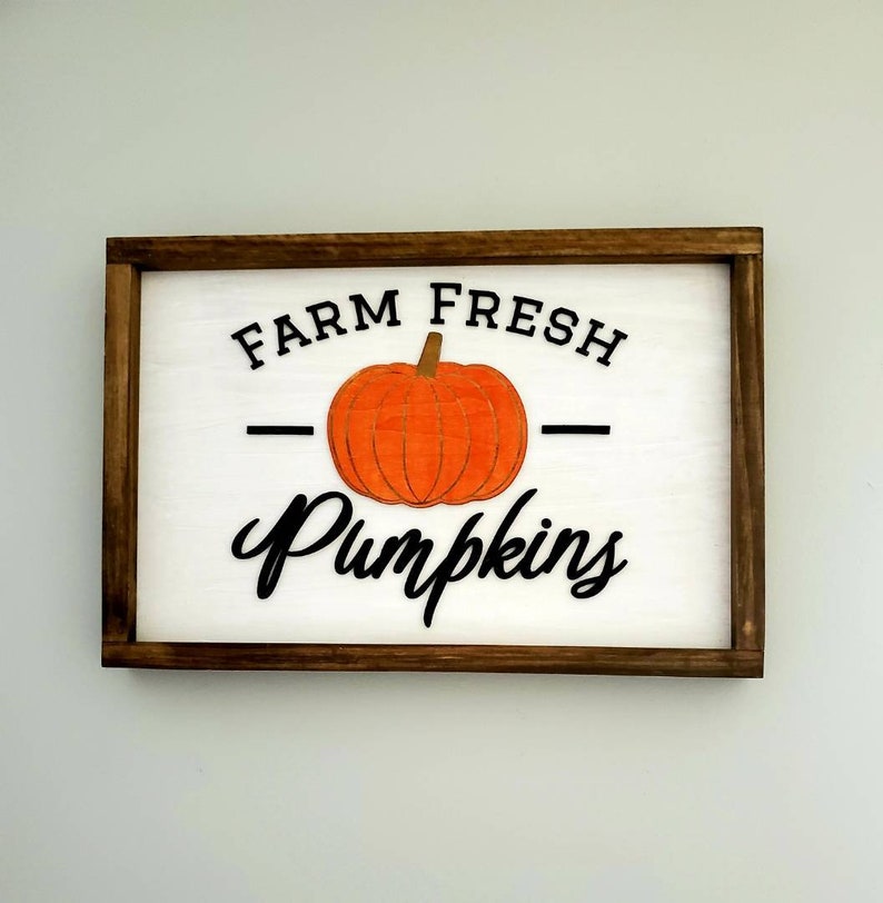 Puede incluir: Un letrero de madera con marco marr&oacute;n y fondo blanco. El letrero dice "Farm Fresh Pumpkins" con una ilustraci&oacute;n de calabaza negra y naranja.