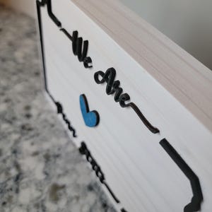 May include: White wooden sign with a black outline of the state of Pennsylvania. The sign says "We Are" with a blue heart in the middle.