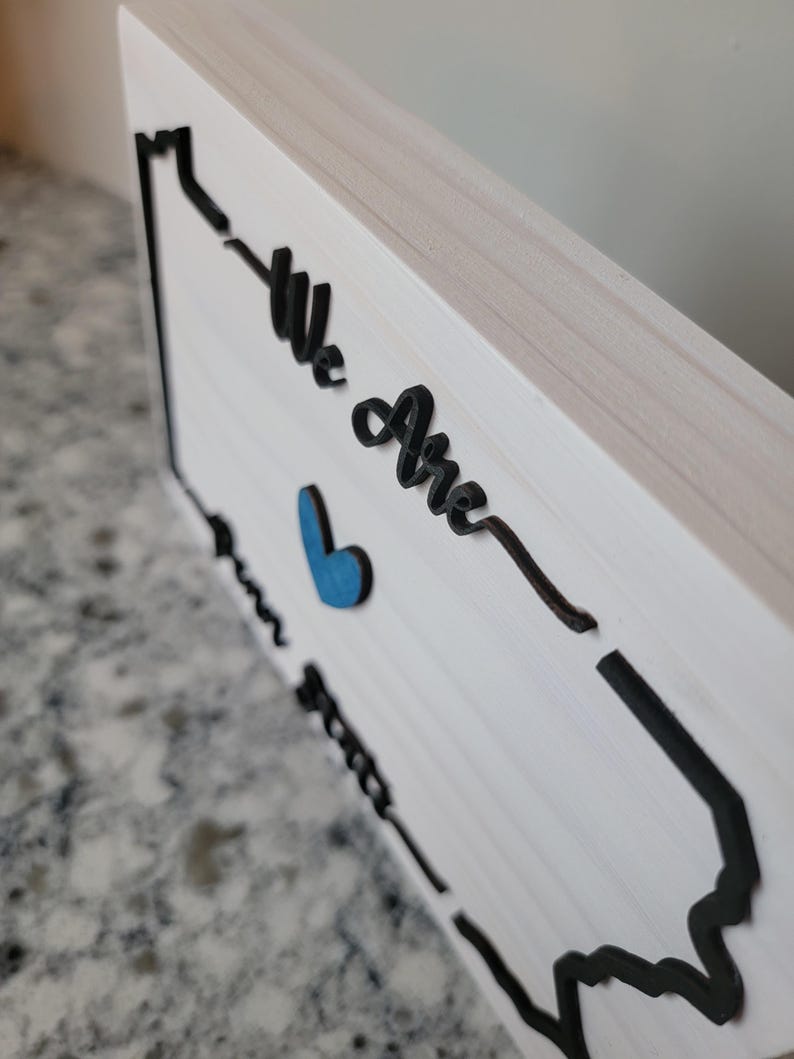 May include: White wooden sign with a black outline of the state of Pennsylvania. The sign says "We Are" with a blue heart in the middle.
