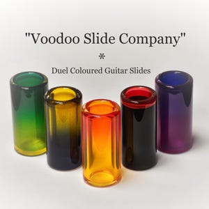 May include: Five dual-coloured glass guitar slides in shades of green, yellow, orange, red, and purple. The text "Voodoo Slide Company" and "Duel Coloured Guitar Slides" are displayed above the slides.