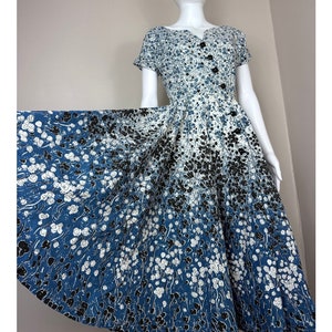 May include: A vintage blue and white floral print dress with a button-up front and short sleeves. The dress has a full skirt and a fitted bodice.