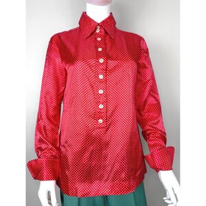 May include: A red long-sleeved button-up shirt with white polka dots. The shirt has a collar and long sleeves with button cuffs.