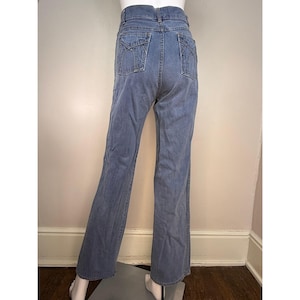May include: Light blue denim jeans with a high waist and flared leg. The jeans have two back pockets with decorative stitching. The jeans are displayed on a mannequin.