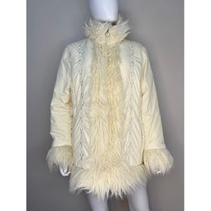 Puede incluir: Abrigo de invierno color crema con detalles de piel sintética. El abrigo presenta un cuello alto, ribete de piel en los puños y la parte delantera, y costuras decorativas. El abrigo se exhibe en un maniquí.