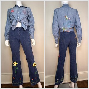 May include: A denim shirt and flared jeans set. The light blue shirt has embroidered details and a tied front. The dark blue jeans feature embroidered flowers and a flared leg. A vintage-inspired outfit.