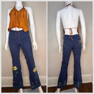 May include: A two-piece outfit featuring a burnt orange halter top and navy blue corduroy pants. The pants have a floral embroidery design at the hem. The top ties at the neck and back.