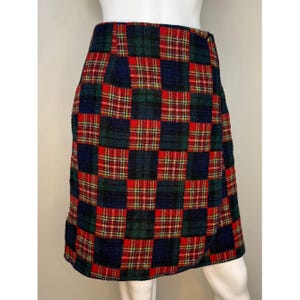 May include: A plaid patchwork skirt in a mini length. The skirt features a mix of red, green, and navy blue plaid squares. The skirt has a wrap-style design with a slight overlap at the front. The fabric appears to be a woven material.