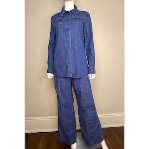 May include: A two-piece denim outfit, comprising a long-sleeved button-down shirt and wide-leg trousers. The shirt features a collared neckline and pocket detailing. The outfit is a medium blue wash and is displayed on a mannequin.