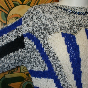 May include: A vintage sweater with a unique design. The sweater features a mix of black, white, and blue knit patterns, with a touch of silver sequins. The design includes stripes and geometric shapes, creating a bold and retro look.