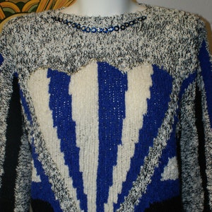 May include: A vintage sweater with a unique design. The sweater features a heart-shaped pattern with blue and white stripes, outlined with silver thread. The upper portion is a mix of black and white knit, with blue sequin detailing around the neckline.