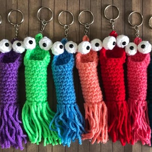 May include: Eight crocheted worm keychains with googly eyes and fringe. The worms are in various colors, including yellow, purple, green, blue, pink, red, and teal.