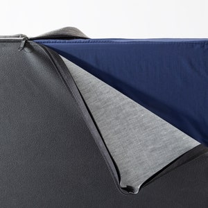 May include: A close-up of a dark gray sofa cushion with a zipper that is partially open, revealing a light gray fabric layer and a dark blue fabric layer underneath.