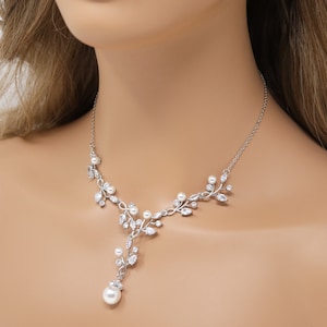 Peut inclure: Un collier en argent avec un délicat motif de vigne orné de petites perles et de strass transparents. Le collier a une goutte de perle pendante.
