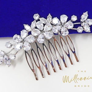 Peut inclure: Un peigne à cheveux argenté avec un motif floral composé de strass transparents. Le peigne a sept dents et est décoré d'un groupe de strass en forme de poire et ronds.