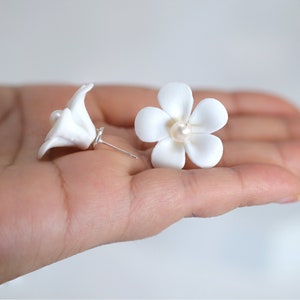 May include: A pair of white flower earrings with a pearl in the center of each flower.
