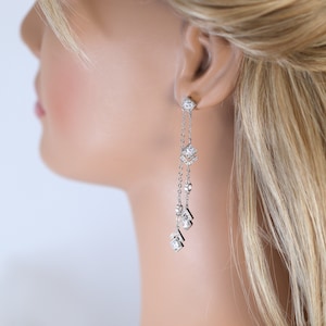 Peut inclure: Boucles d'oreilles pendantes en argent avec plusieurs petites pierres de zircone cubique transparentes. Les boucles d'oreilles ont un design délicat en chaîne.
