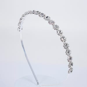 Peut inclure: Un serre-tête argenté orné d'une rangée de strass clairs et étincelants. Les pierres décoratives sont espacées sur le dessus du bandeau, créant un accessoire glamour. Idéal pour les événements spéciaux.
