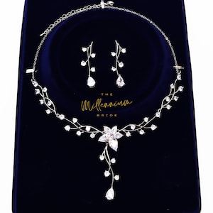 Peut inclure: Un ensemble de collier et boucles d'oreilles de mariée en argent avec un motif floral et des cristaux transparents. Le collier présente un pendentif de fleur tombant avec un cristal en forme de larme au bas. Les boucles d'oreilles sont simples et présentent un seul cristal en forme de larme.
