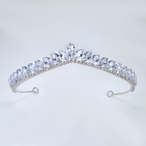 Peut inclure: Un diadème argenté orné de pierres précieuses claires, de taille marquise. Le diadème présente un design incurvé avec un pic central et des boucles aux extrémités. Les pierres sont serties en rangée le long de la bande du diadème.