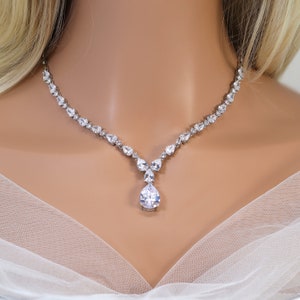 May include: A silver necklace with a teardrop-shaped pendant set with clear cubic zirconia stones. The necklace is made of a delicate chain and features a cluster of smaller stones at the base of the pendant.