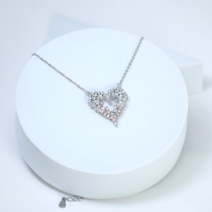 May include: A silver necklace with a heart-shaped pendant made of small, clear and pink crystals.