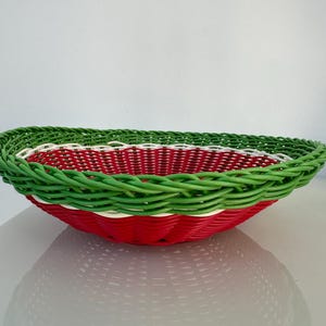 May include: A colourful woven basket. The basket has a red base, a white middle section, and a green rim. The basket is round and has a woven texture. The basket is likely made of wicker or a similar material.