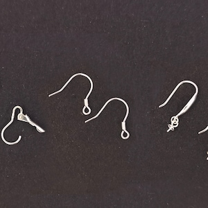 May include: Five silver earring hooks on a black background. The hooks are different styles, including a leverback, a French hook, and a fish hook.