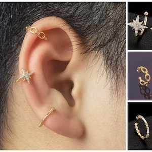 May include: A set of gold ear cuffs featuring a star design with clear rhinestones and a chain link design. The ear cuffs are shown on a person's ear.