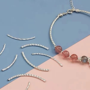 Puede incluir: Un brazalete de plata con un dije de luna creciente y cuentas de piedras preciosas rosadas y grises. El brazalete está sobre un fondo azul y rosa con cuentas espaciadoras plateadas.