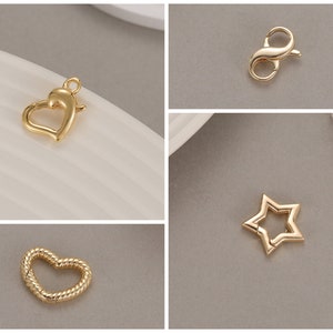 May include: Four gold-toned metal jewelry findings: a heart, a star, a heart with a twisted design, and a lobster clasp.