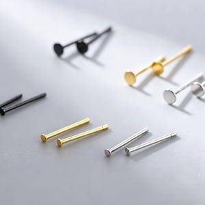 Könnte beinhalten: Eine Sammlung von Ohrsteckern mit flachem Kopf in Schwarz, Gold und Silber. Jeder Ohrstecker besteht aus einem dünnen, geraden Stift und einem runden, flachen Kopf. Der Text G3:ST925S134, B3:ST925S133, B1.5:ST925S138, G1.5:ST925S139 ist in der Ecke aufgedruckt.