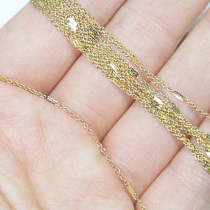 May include: Close-up of a delicate gold necklace with multiple strands. The necklace features a fine chain design with small, rectangular accents. The gold colour is bright and shiny, reflecting light.