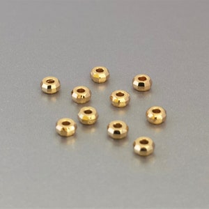 May include: A collection of ten small, gold-colored, faceted beads. Each bead has a cylindrical shape with a hole through the center. The beads are scattered on a light gray surface.