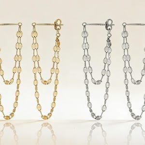 May include: Two pairs of dangle earrings. One pair is gold-toned, and the other is silver-toned. Each earring features a post and two strands of connected, oval-shaped beads that hang down.