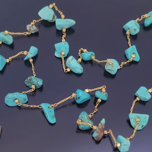 Puede incluir: Un collar largo de cadena de oro con piedras turquesa. Las piedras son de forma y tamaño irregulares, y están enhebradas en una delicada cadena de oro.