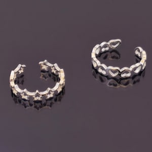 May include: Two silver adjustable rings. One ring features a star design, and the other has a heart design. The rings are open-ended, allowing for size adjustment. The rings are displayed on a dark, reflective surface.
