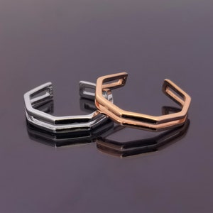 May include: Two geometric rings, one silver and one rose gold, are stacked on top of each other. The rings are made of a double band and have a hexagonal shape.