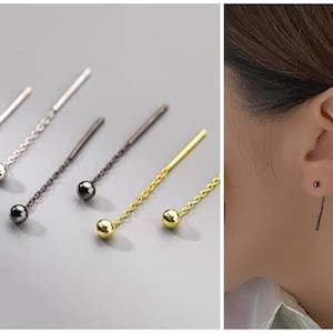Op de afbeelding: Vijf paar delicate kettingoorbellen met kleine bolvormige bedels. De oorbellen zijn verkrijgbaar in goud, zilver en zwart.