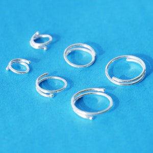 May include: Six silver rings on a blue background. The rings are all double-banded and have a simple, minimalist design.