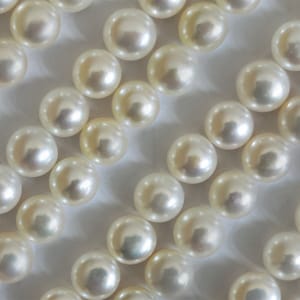 Könnte beinhalten: Nahaufnahme von zahlreichen cremeweißen Perlen. Jede Perle ist rund und hat eine glatte, reflektierende Oberfläche. Die Perlen sind eng aneinandergereiht und bilden ein Muster. Ein klassisches Schmuckaccessoire.