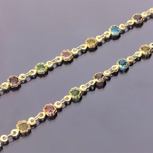 May include: A gold chain necklace featuring colourful gemstones. The chain is made up of small, linked circles with a gemstone in each circle. The gemstones are in a rainbow of colours, including red, orange, yellow, green, blue, and purple.