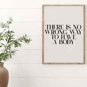 Puede incluir: Una impresi&oacute;n enmarcada con el texto "THERE IS NO WRONG WAY TO HAVE A BODY" en letras negras sobre un fondo blanco. La impresi&oacute;n est&aacute; colgada en una pared blanca con un marco de madera.