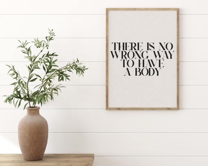 Puede incluir: Una impresi&oacute;n enmarcada con el texto "THERE IS NO WRONG WAY TO HAVE A BODY" en letras negras sobre un fondo blanco. La impresi&oacute;n est&aacute; colgada en una pared blanca con un marco de madera.