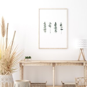 May include: A framed watercolor print of four stylized trees in shades of green and gray on a white background. The print is hanging on a white wall above a wooden console table with a wooden sign that reads "HOME".